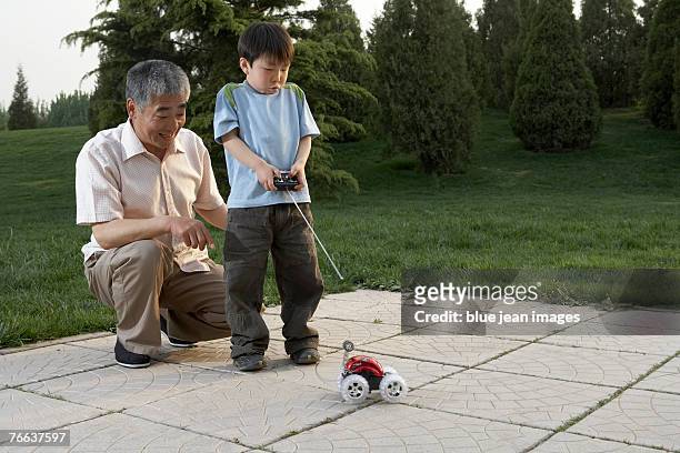 an old man and a boy are playing with a remote control car. - car remote toy fotografías e imágenes de stock