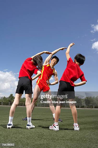 a track and field athlete is guiding two kids to do exercises. - portrait of school children and female teacher in field stock pictures, royalty-free photos & images
