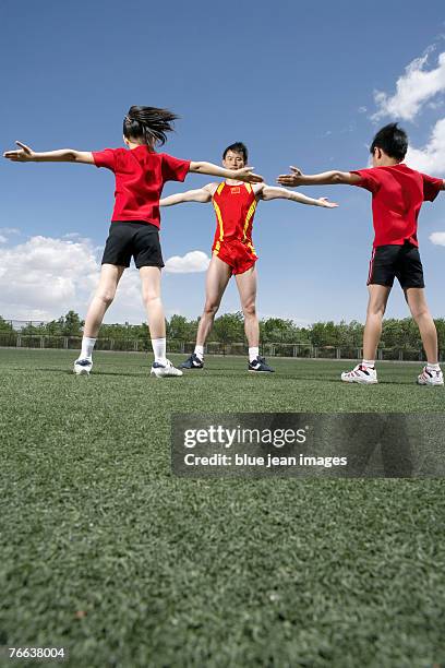 a track and field athlete is guiding two kids to do exercises. - portrait of school children and female teacher in field stock pictures, royalty-free photos & images