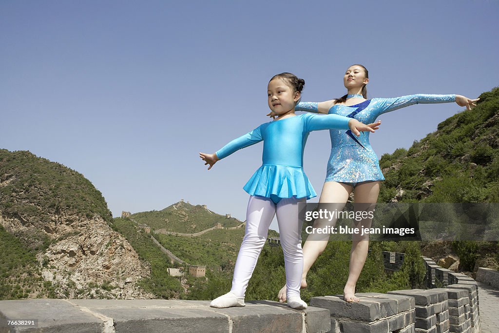 A young girl and an athlete practicing gymnastics on the Great Wall of China.