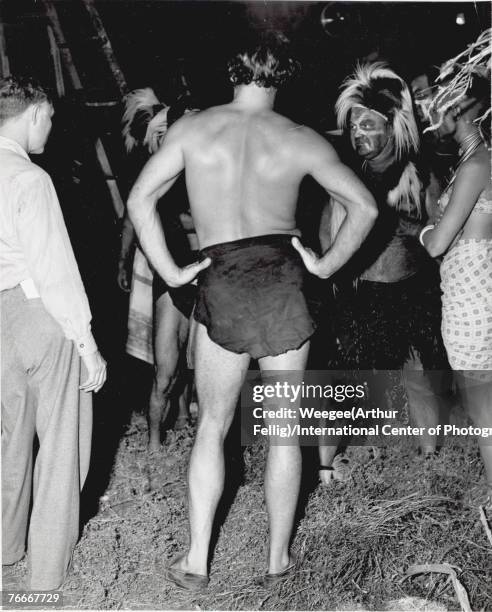 American actor Lex Barker stands with his hands on his hips in his Tarzan loincloth during a break in filming, late 1940s or early 1950s. Barker...