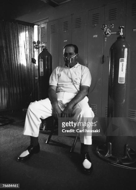 American golfer Claude Harmon sits on a chair in a locker room at Cherry Hills Country Club, and uses an oxygen inhalator after playing 18 holes in...