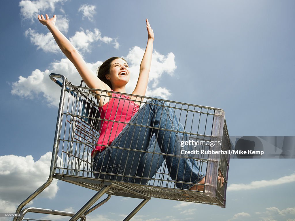 Woman in shopping cart outdoors with arms up smiling