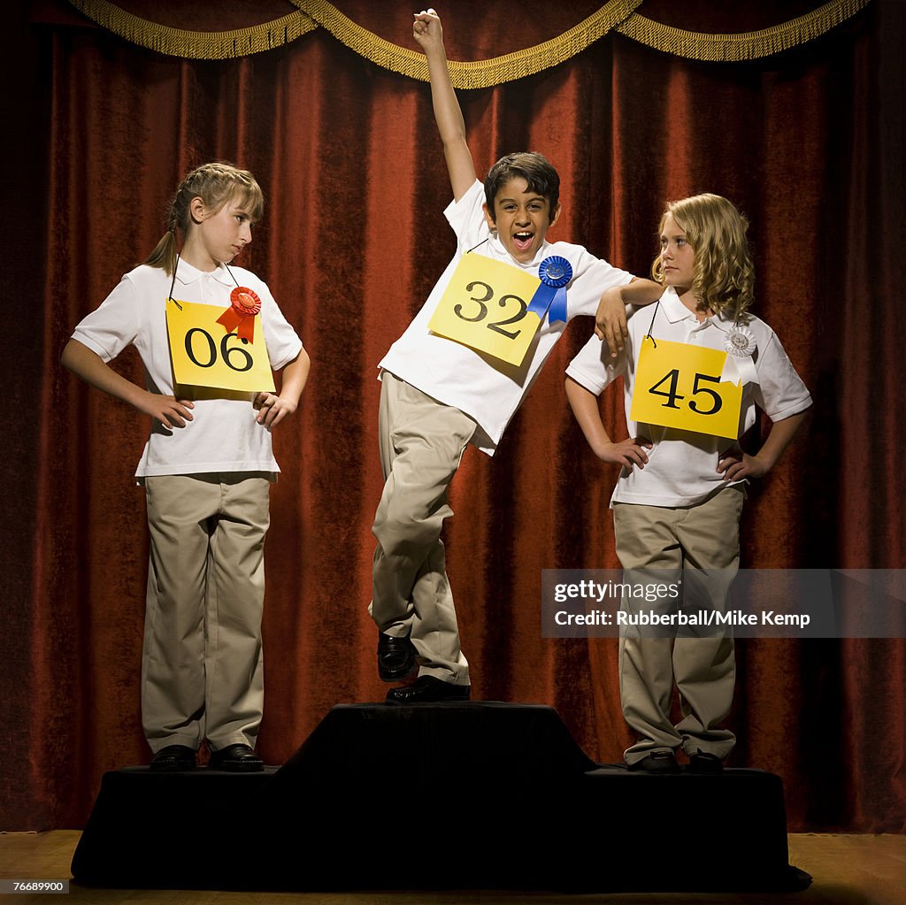 Three children on stage at winner's podium with ribbons smiling