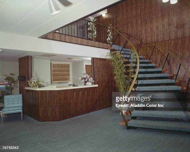 View of the lobby of the Sting Ray Motel, which contains a wood-panelled front desk and a wide, curved staircase, Ocean City, New Jersey, 1960s. A...
