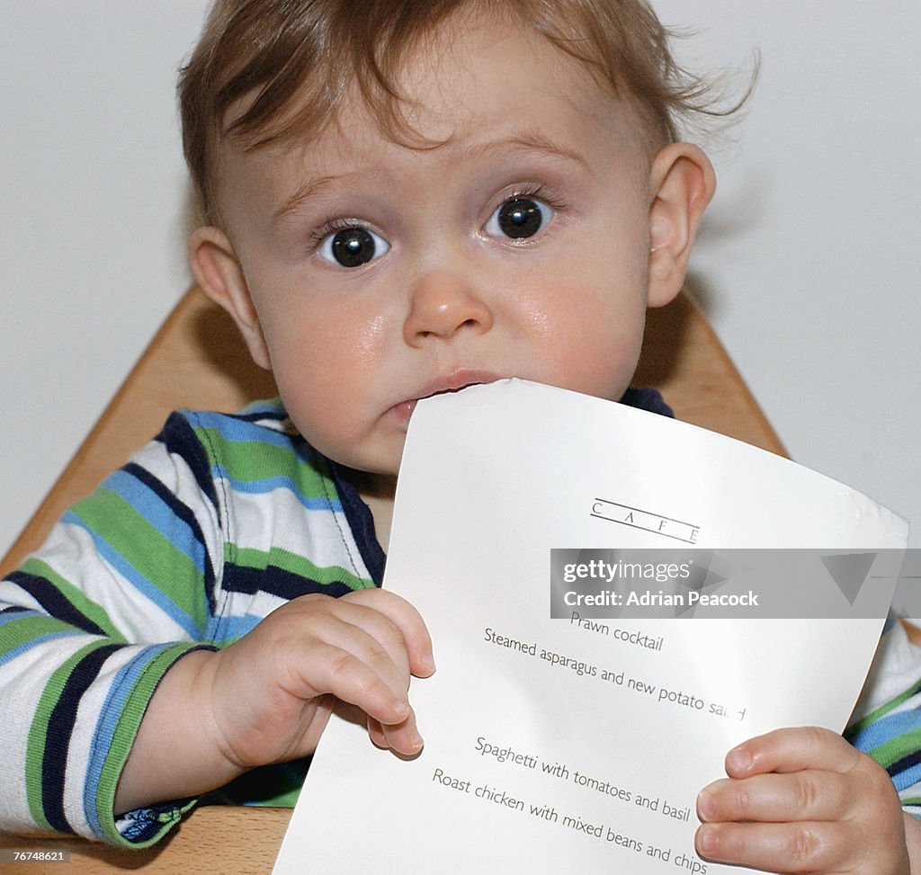 Toddler boy chewing on a menu