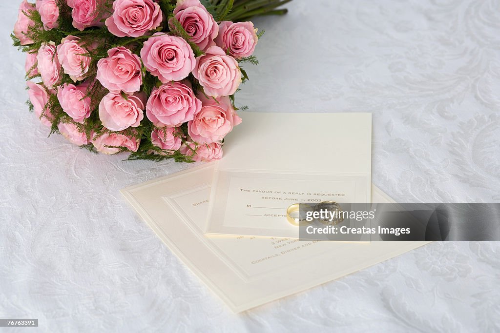 Wedding bouquet of pink roses and wedding rings on invitation