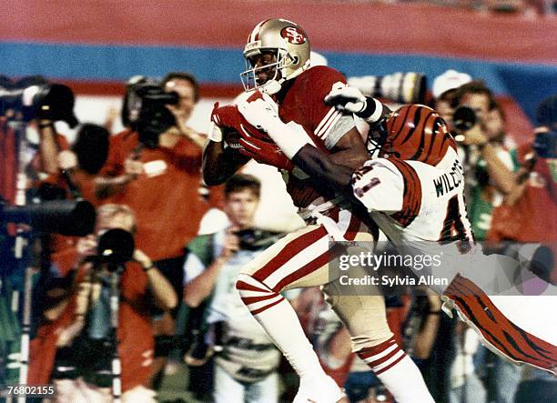 San Francisco 49ers wide receiver Jerry Rice runs with the football after making a catch and drags Bengals defensive back Solomon Wilcots along the...