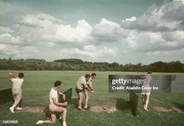 Group of men golf on a driving range on the grounds of the Riverside Hotel, Divine Corners, New York, 1950s or 1960s. In the center, one golfer's...