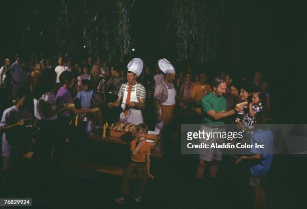 Night time view of Pine Lake Manor hotel guests as they eat hot dogs and listen to music at an outdoor event, Greenville, New York, mid to late 1960s.