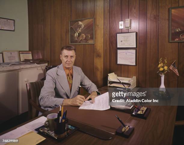 An unidentified medical administrator signs paperwork in a wood-panelled office in the New Horizon Rehabilitation Center, Ocala, Florida, 1960s.