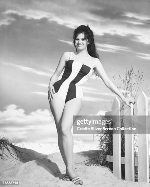 Italian actress Claudia Cardinale models a striped swimsuit on the beach, circa 1965.