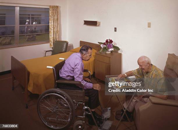 Two elderly men, one in a wheelchair, play a game of Chinese checkers in a residential room at an unidentified medical facility, 1960s.