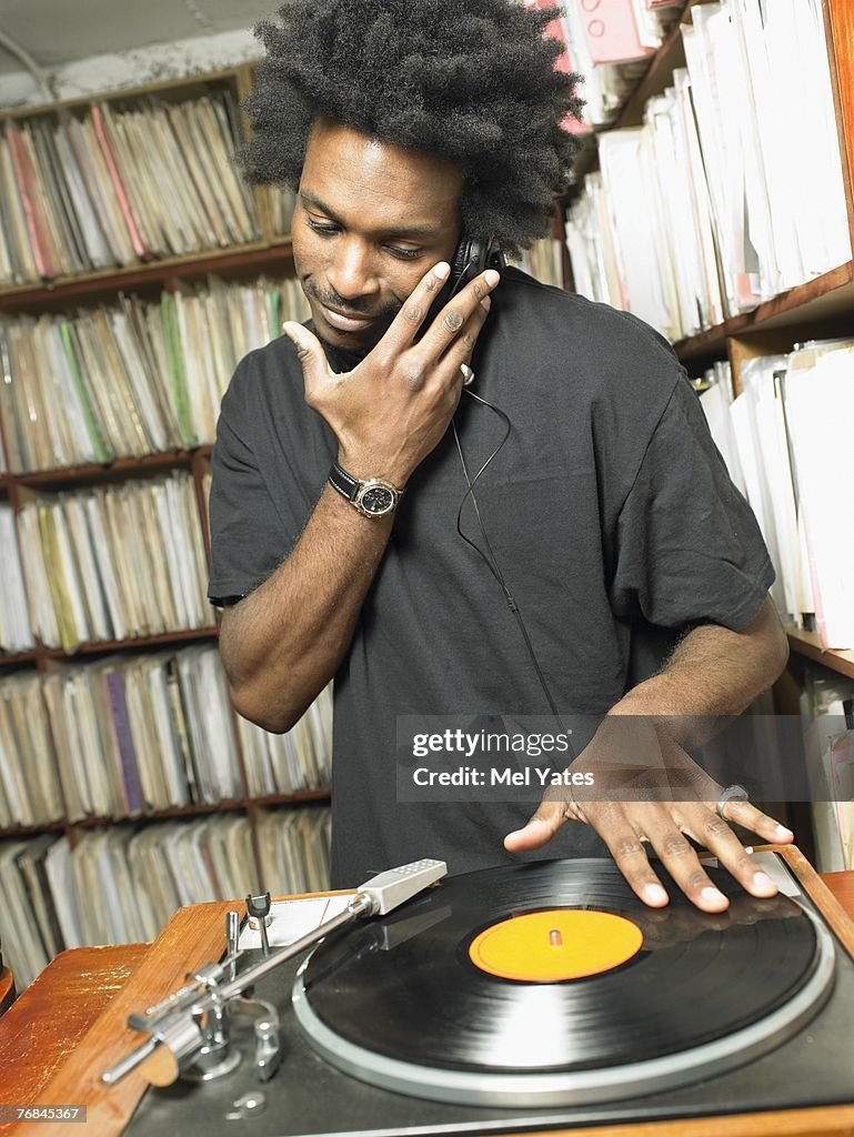 Male DJ playing record in music shop, smiling