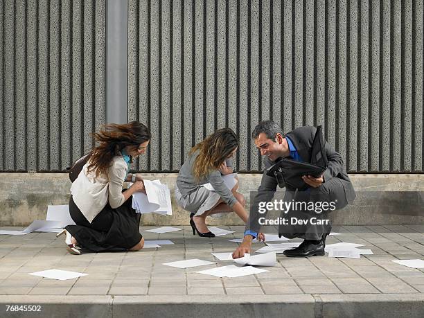 two businesswomen and one businessman trying to recover papers blowing about pavement, alicante, spain, - skirts blowing up 個照片及圖片檔