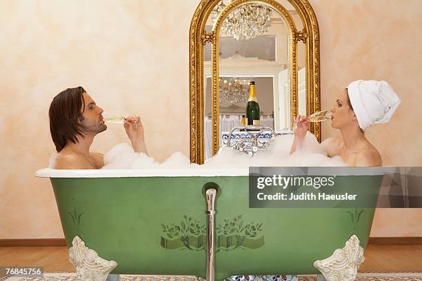 young couple sitting in bath drinking champagne, side view - couple bathtub photos et images de collection