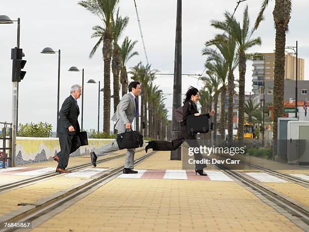 businesswoman and two businessmen running acrossdouble tram lines with suitcases at zebra crossing. alicante, spain. - zebrastreifen stock-fotos und bilder