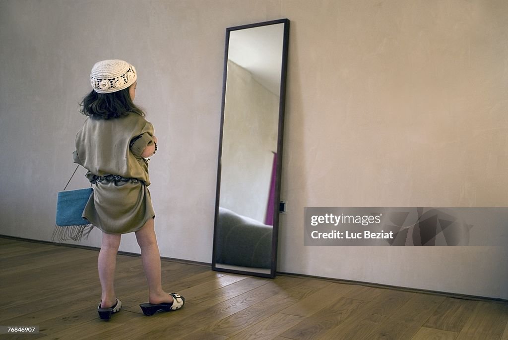 Girl (2-4 years) dressing up for party, posing in mirror.