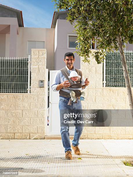 father looking at camera with 5 month old baby in sling, urban location, alicante, spain, - baby carrier stock pictures, royalty-free photos & images