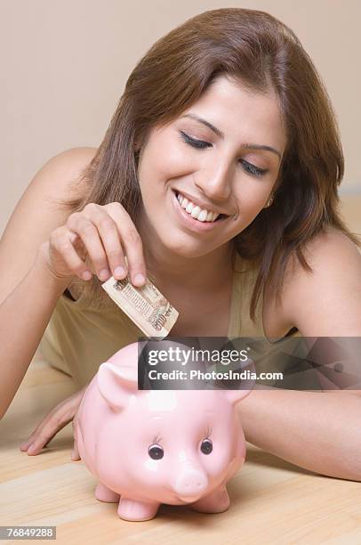 close-up of a young woman inserting money into a piggy bank - indian rupee note stock pictures, royalty-free photos & images