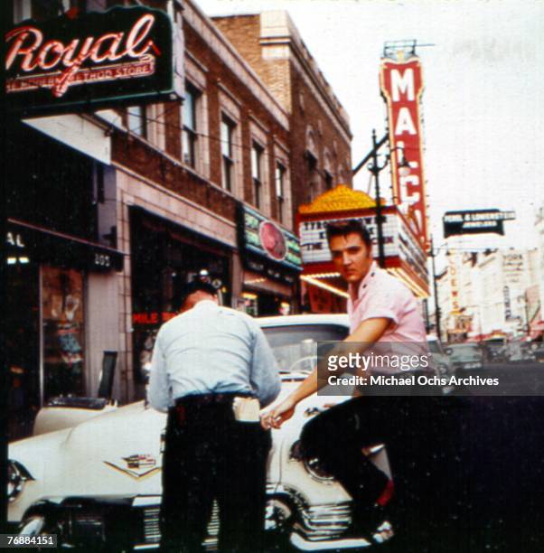 Singer Elvis Presley leans against his Cadillac as he gets a parking ticket on Main Street outside of Jim's Barber Shop in 1956 in Memphis, Tennessee.
