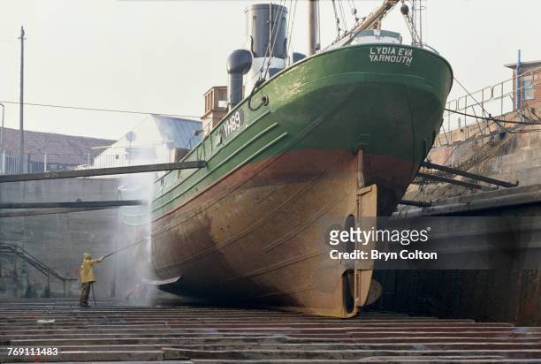 Workmen using water pressure hoses to clean the hull of the Lydia Eva YH89, in dry-dock at Lowestoft, Suffolk, 12th October 1990. The ship is the...