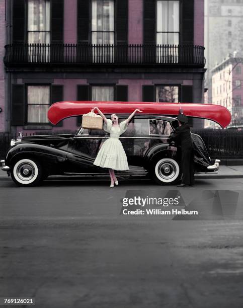 American model Barbara Mullen, in a pale green dress, pose with her arms in the air, a picnic basket in one hand, as she stands in front of a black...