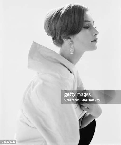 Three-quarter profile portrait of American model Kathy Ainsworth dressed in a white, broad-collared jacket and pearl earrings, New York, New York,...