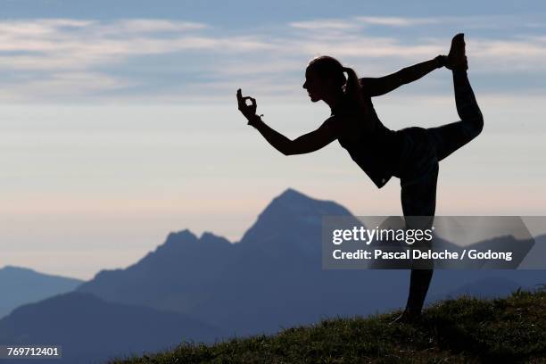 a woman performs a hatha yoga pose on a mountain top. natarajasana: lord of the dance. french alps. france. - lord of the dance pose stock pictures, royalty-free photos & images