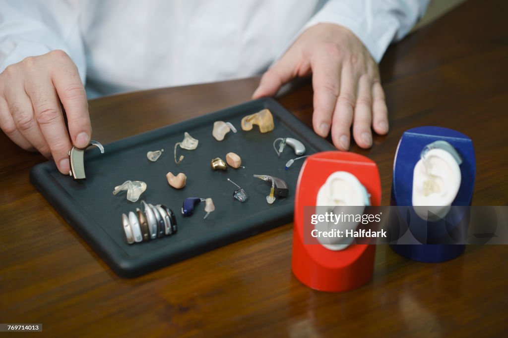 Midsection of audiologist various hearing aids at table in doctors office