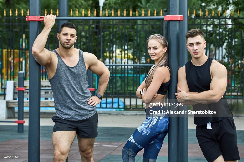 Portrait of confident young athletes standing by horizontal bar