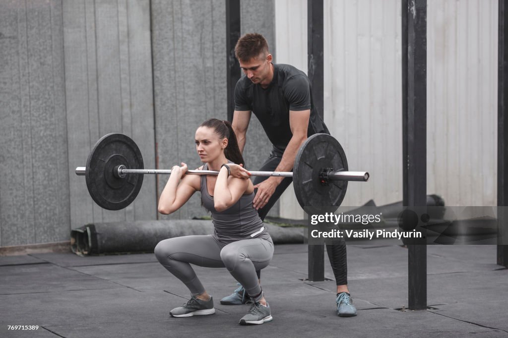 Male instructor assisting young woman gym training at gym