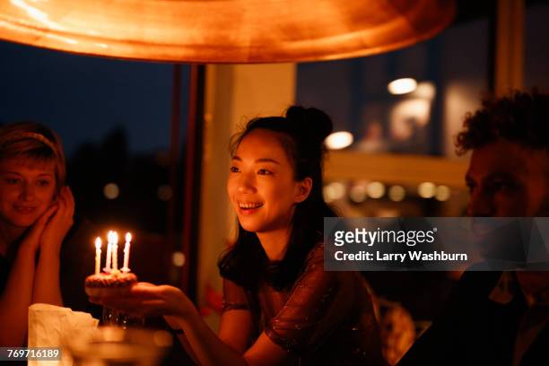 happy woman holding small birthday cake with lit candles while sitting by friends at home - life events ストックフォトと画像