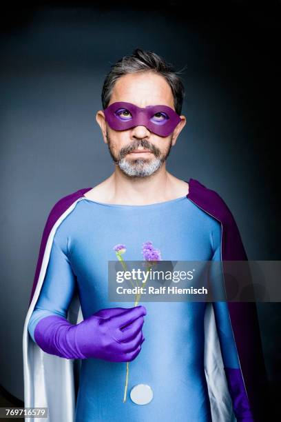 portrait of man dressed as superhero holding flower against gray background - purple glove stock-fotos und bilder