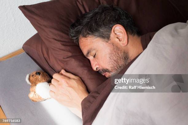 high angle view of mature man sleeping by small teddy bear on bed at home - teddy day stockfoto's en -beelden