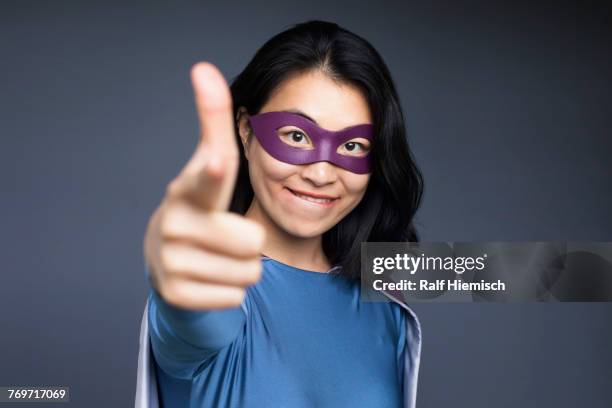 portrait of smiling female superhero pointing against gray background - heldin stock-fotos und bilder