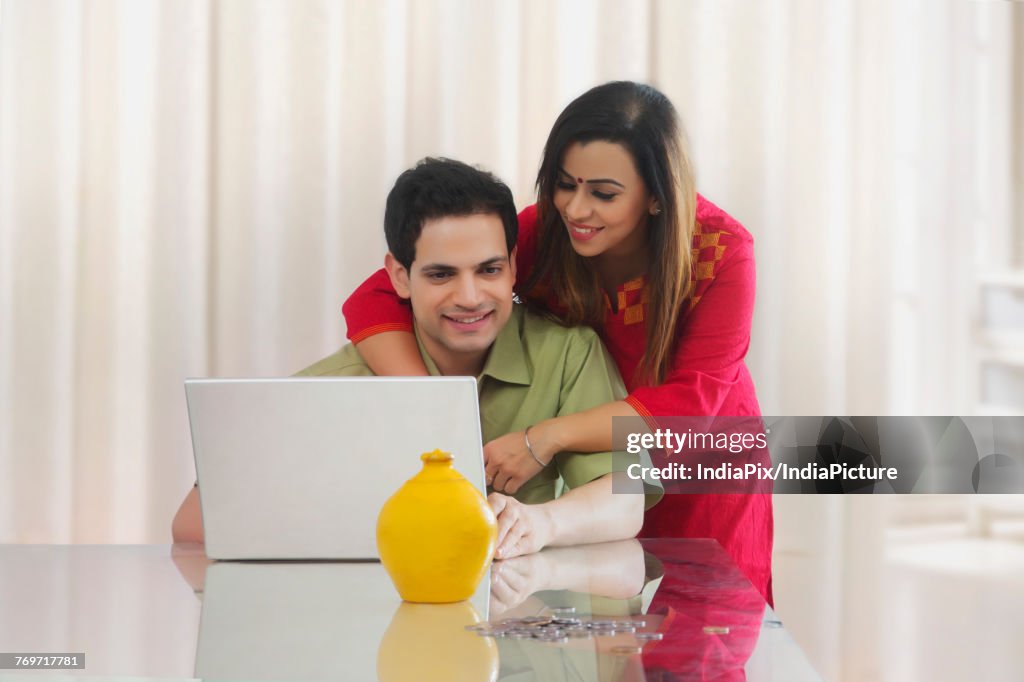 Couple looking at laptop with coins and piggy bank on table