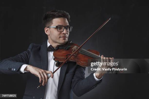 smiling handsome violinist playing violin against black background - geigerin stock-fotos und bilder