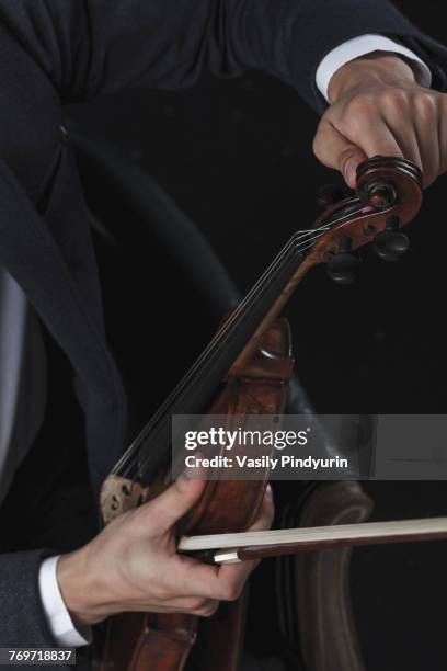 cropped image of violinist tuning violin while sitting on chair - tuning peg stock pictures, royalty-free photos & images