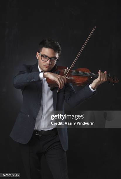 confident musician playing violin while standing against black background - tuning peg stock pictures, royalty-free photos & images