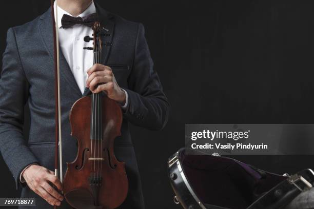 midsection of man holding violin while standing by case against black background - tuning peg stock pictures, royalty-free photos & images