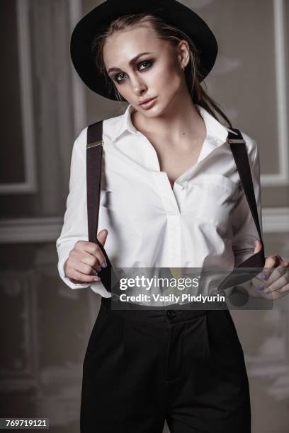 portrait of young woman wearing suspenders standing against wall - women in suspenders stock-fotos und bilder