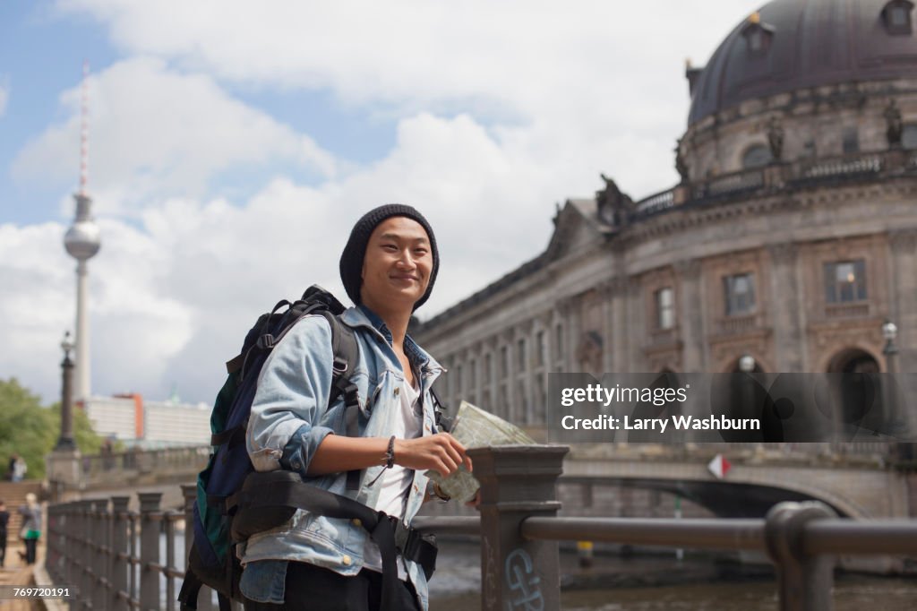 Smiling young male tourist standing with map by railing against Bode Museum, Berlin, Germany