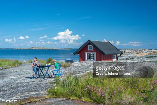 mother and son sitting at rocky coast - cottage water stock pictures, royalty-free photos & images