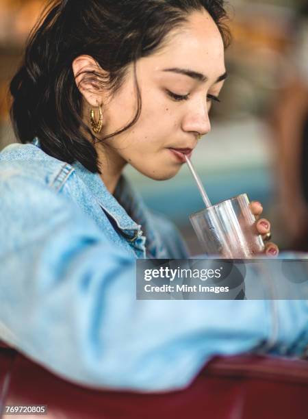 young woman sitting at a bar counter, holding a glass, drinking with a straw. - straw ストックフォトと画像