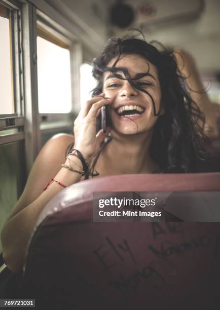 Young woman sitting on a school bus holding a mobile phone to her ear.