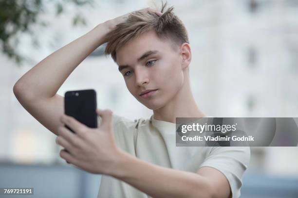 teenage boy taking selfie from mobile phone with hand in hair - male hair hand ストックフォトと画像
