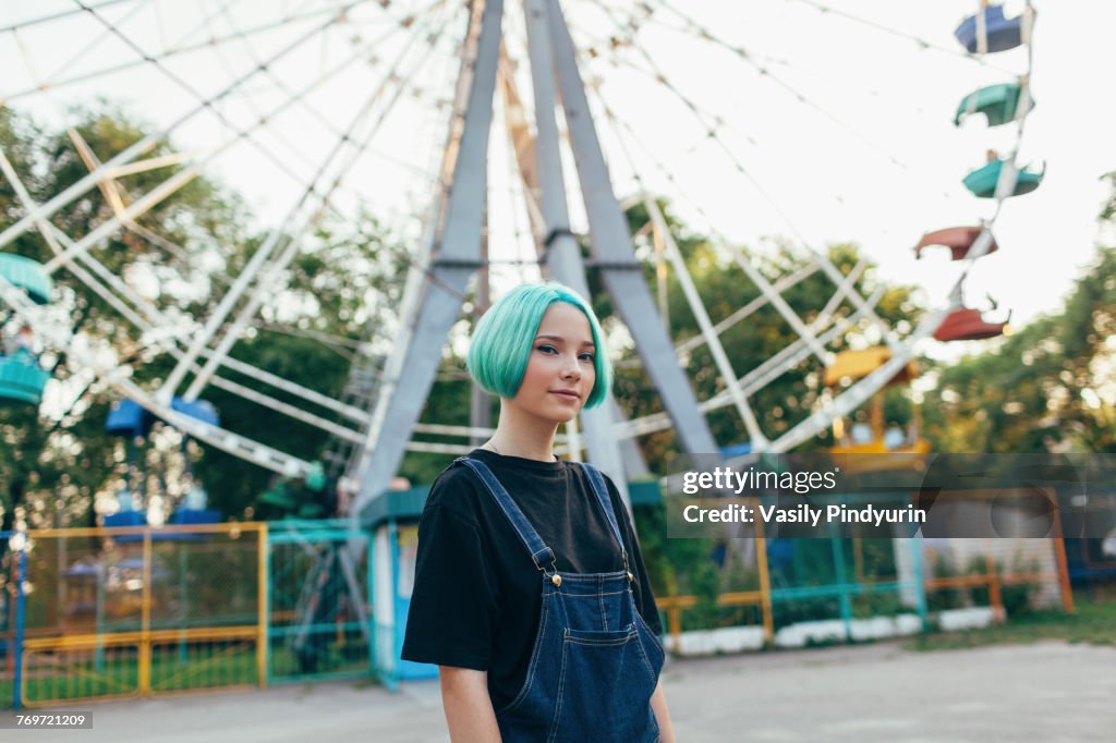 Portrait of smiling teenage girl standing against Ferris wheel at park