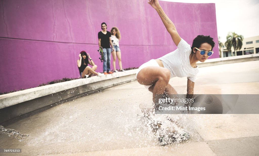 A young woman crouching down on a skateboard to create a water spray.