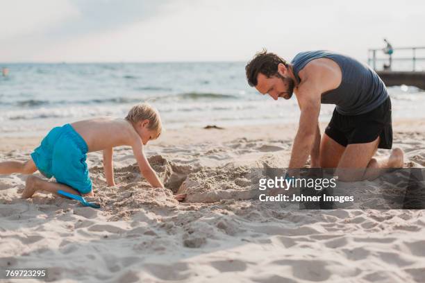 father playing with son on beach - creuser photos et images de collection